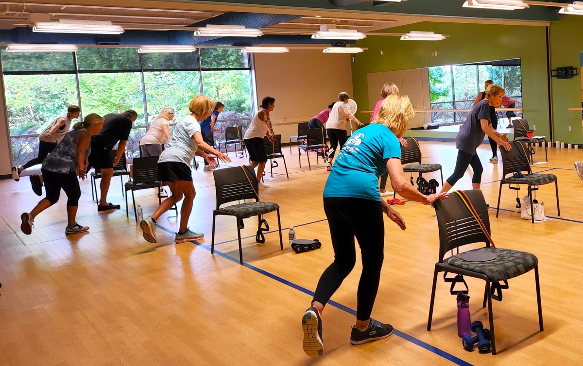Group of people exercising with chairs in a dance studio room. 
