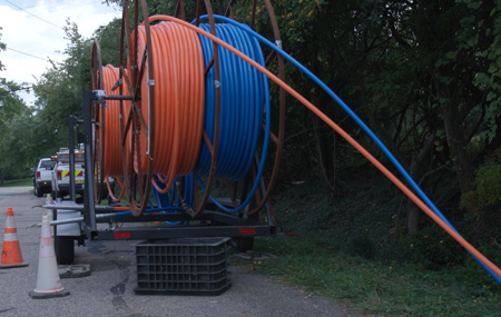 Spools of red and blue cables on a trailer parked by construction cones and utility trucks.