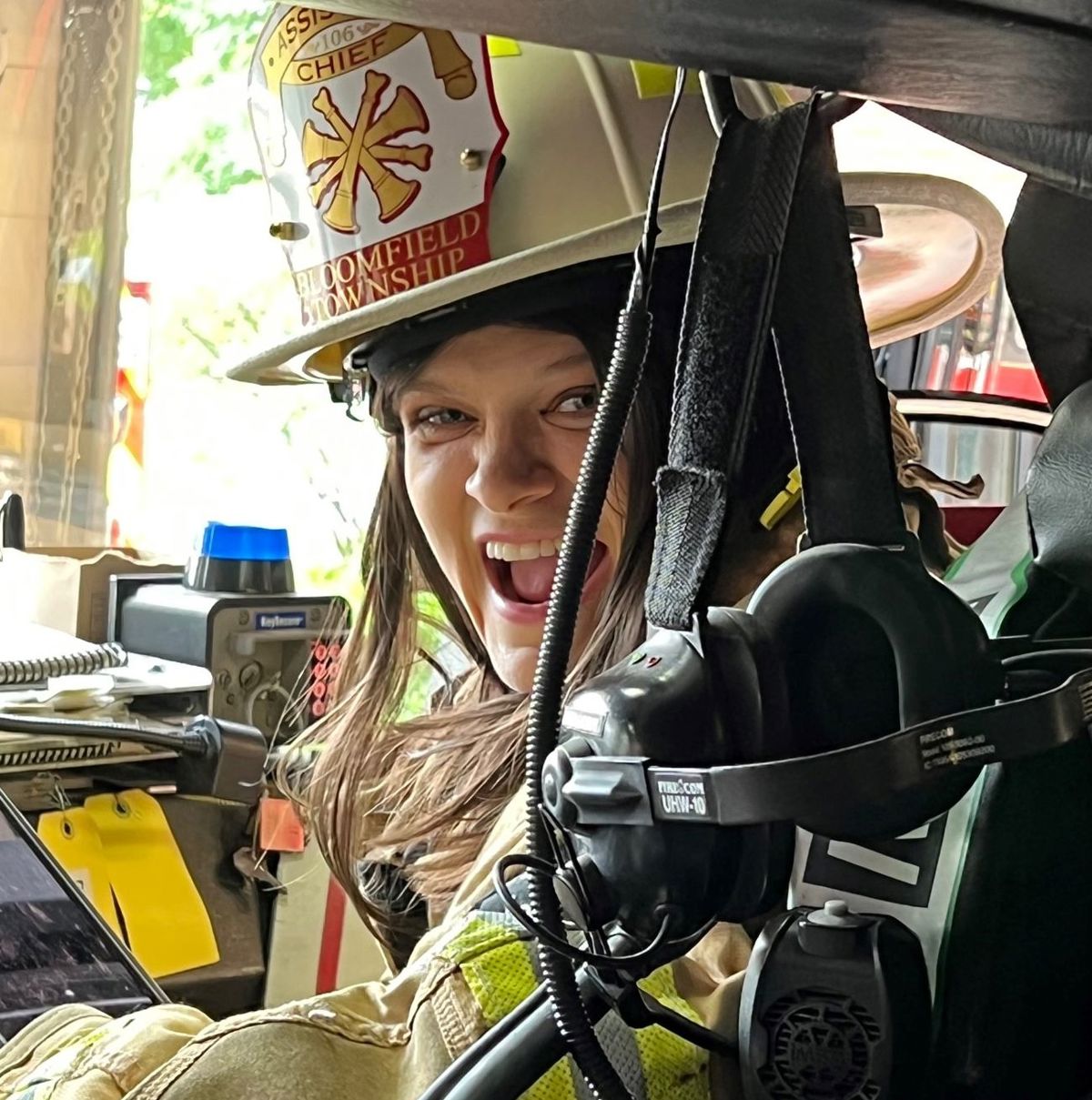 Woman sitting in a fire truck with firefighting gear on. 