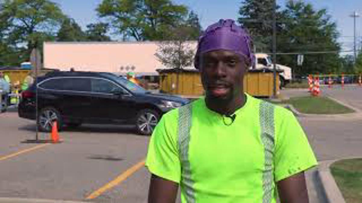 A man with a safety shirt standing in a parking lot. 