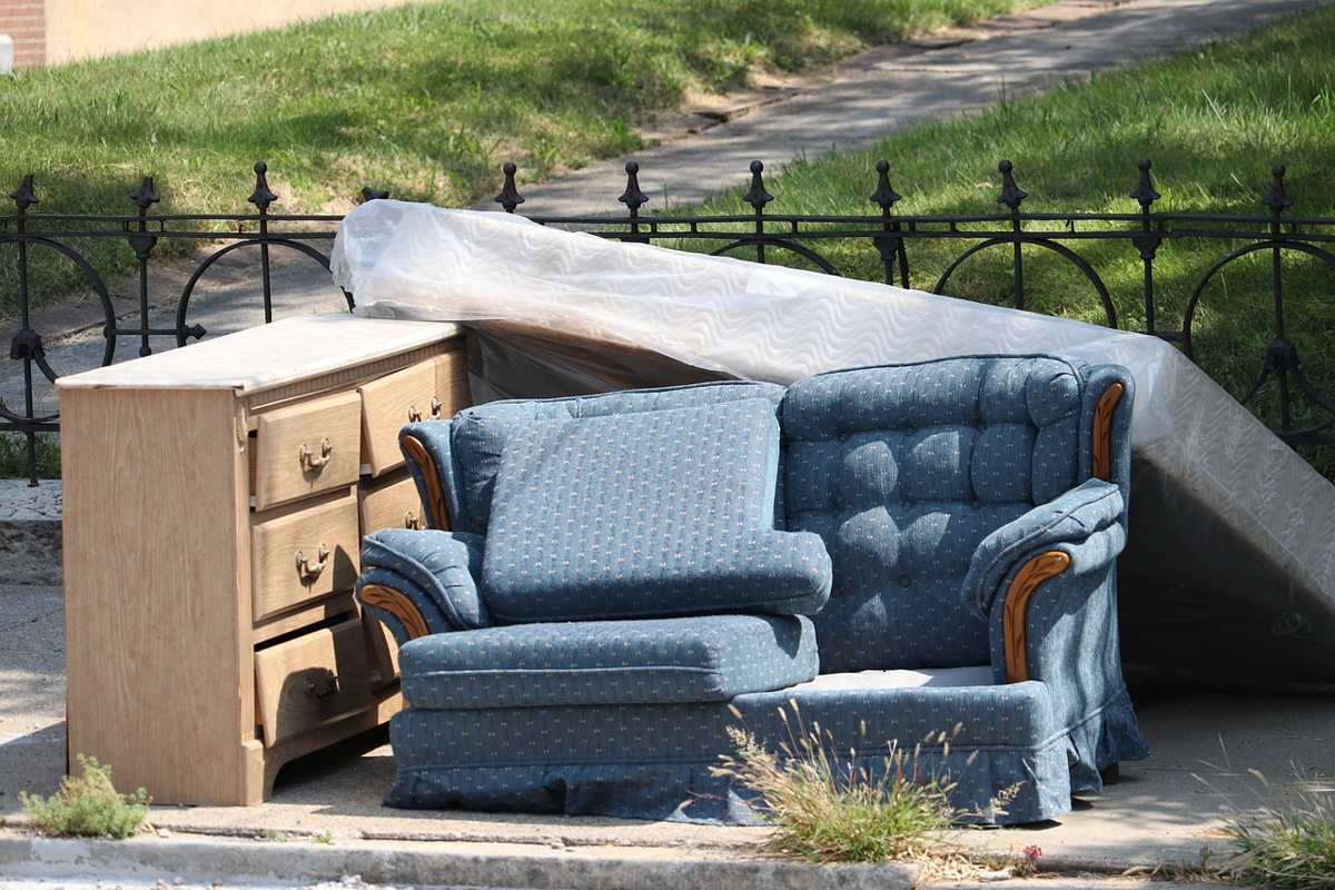 An old dresser, couch, and mattress on the curb of a street. 
