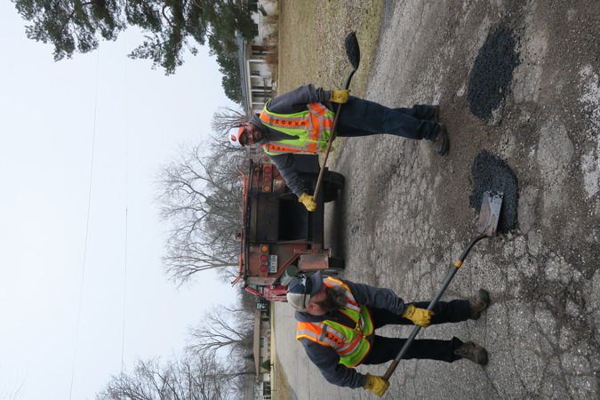 Two public works personnel filling potholes on a residential road